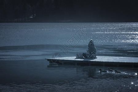 坐在湖边的木头码上在阳光明媚的冬天在斯洛维尼亚水中流血图片