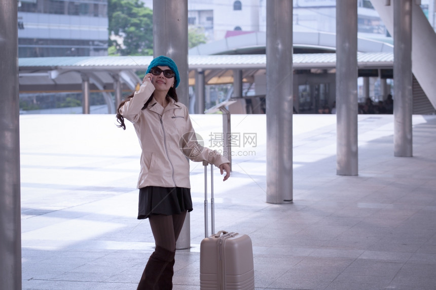身穿毛衣带行李的蓝纱帽在购物商行街头背景打电话作为旅行者度假游概念的亚洲行妇女图片