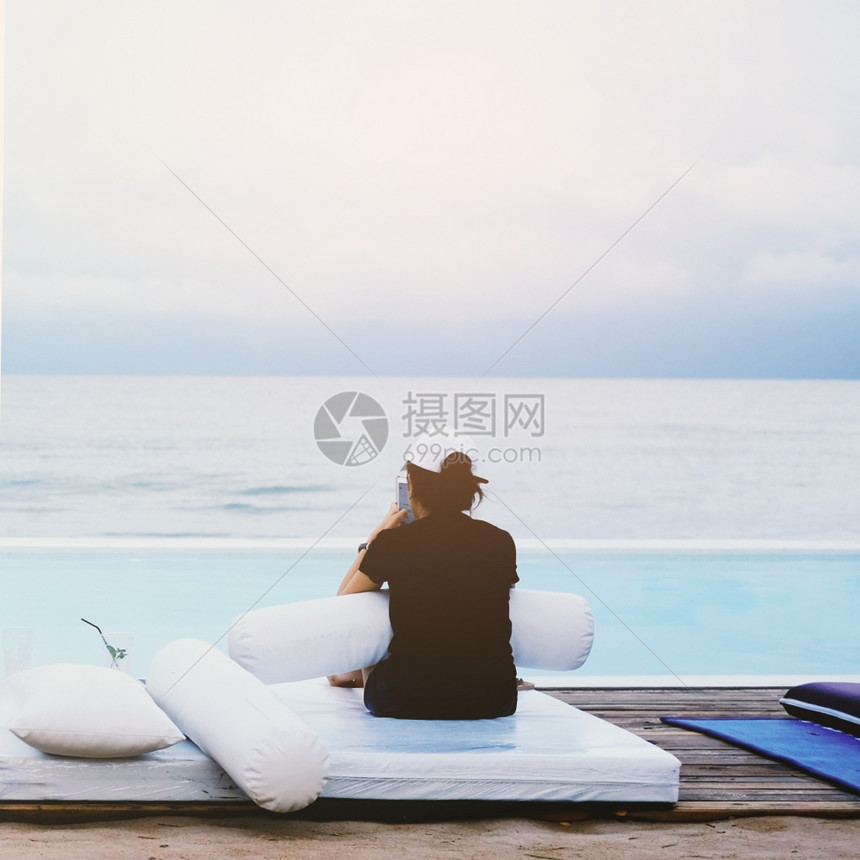 在度假暑概念的游泳池床上使用智能手机的年轻妇女图片