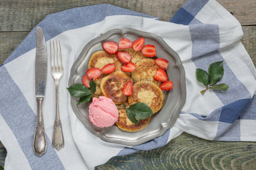 盛夏早餐煎饼加冰淇淋和成熟的草莓放在古董锡板上用旧刀和叉子顶视图片