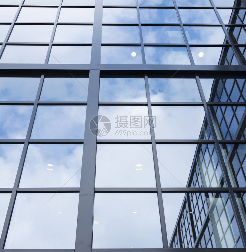 蓝色天空的反射云层和其他建筑在现代办公大楼的玻璃面罩下图片