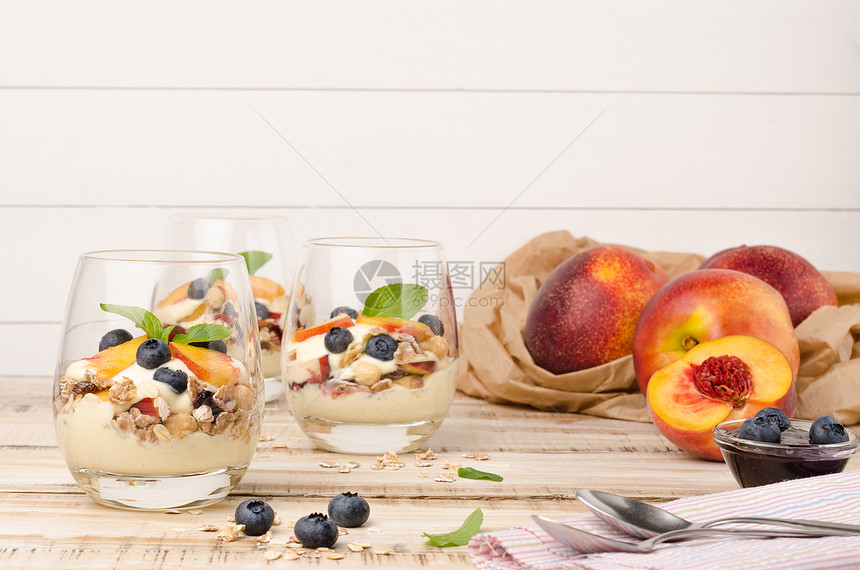 木制桌上有桃子酸奶和蓝莓的颗粒图片