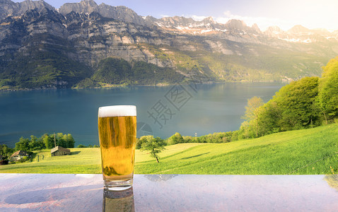 在阳光明媚的夏日紧贴上一杯啤酒桌子上摆放的是阿尔卑斯山脉绿地和背景中的瓦伦西湖背景图片