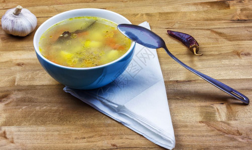 一碗汤和金属勺子放在餐桌上图片