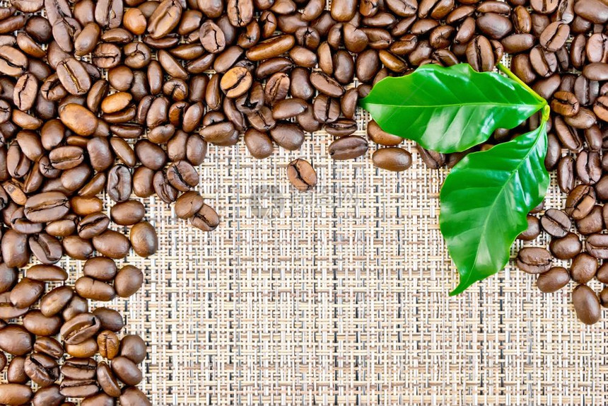 黑咖啡豆框架和棕粗织布上的绿叶子图片