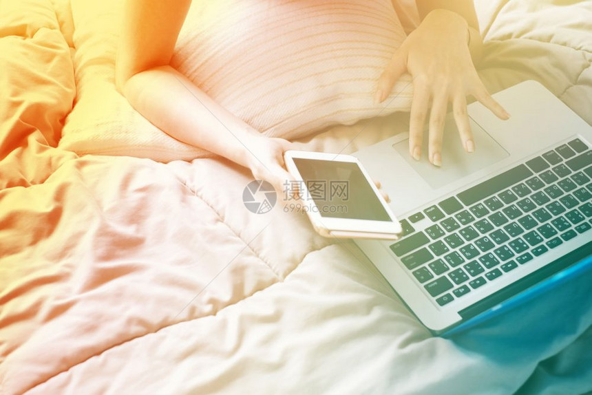特写女人懒洋洋地躺在床上拿着笔记本电脑和智能手机色彩过渡风格和渐变色图片
