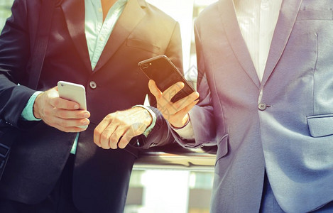 在现代办公大楼商业和技术概念之外使用智能手机的两名同业商人中间部图片