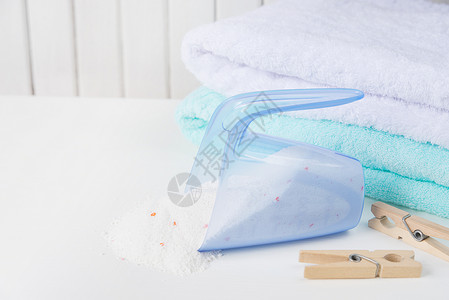 白色浴巾白色和蓝毛浴巾堆叠成白和蓝色毛浴巾从测量杯和木制衣板底白色面的木上洒落洗衣粉背景