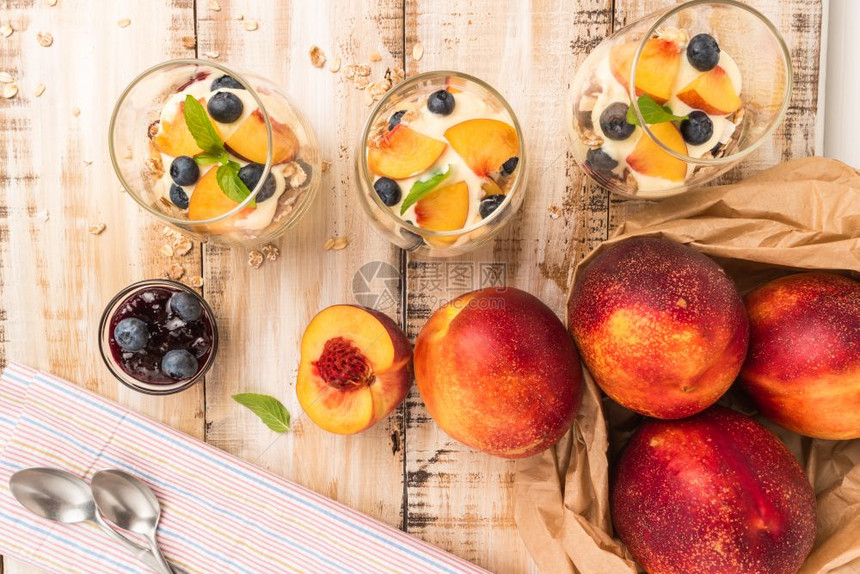 木制桌上有桃子酸奶和蓝莓的颗粒图片