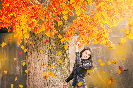 穿着黑色夹克到达多彩的树枝看着落叶享受秋天的气氛图片