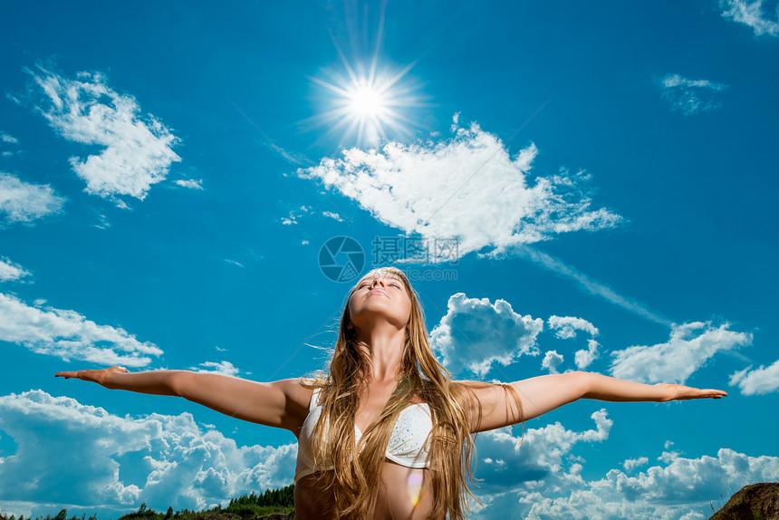 美丽的女人手臂伸展在太阳和天空的背景在比基尼的图片