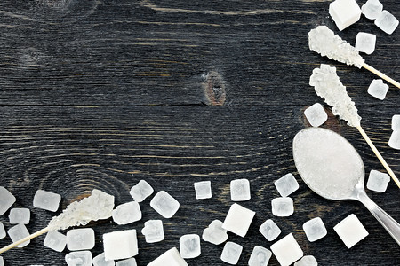 勺子立方和晶体中的糖白颗粒以黑木板背面的框形式在木棍上的子图片
