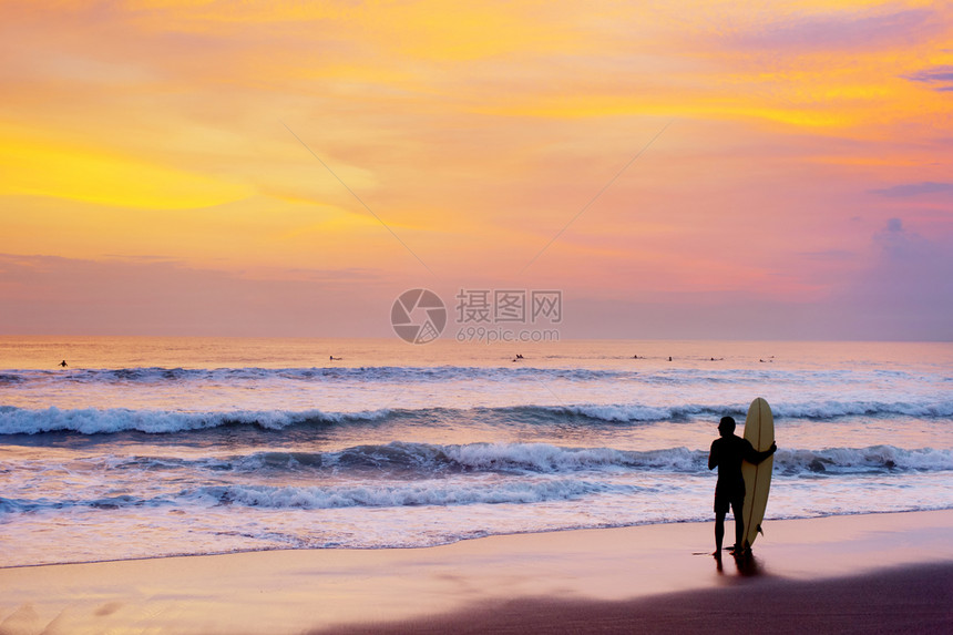 日落时冲浪者与板一起停留在海滩上图片