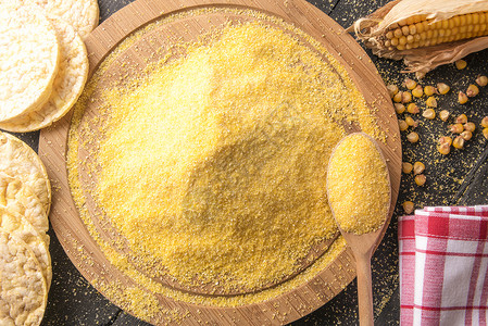 圆木板上有一堆玉米面粉的高角图象环绕在黑木板上有玉米鳕谷物和花粉玉米饼背景图片