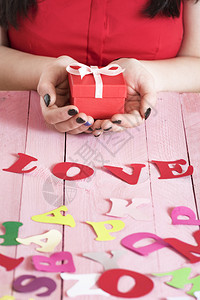 女人手握着一个红礼盒在粉色的木制桌子上满是多色纸字母和面的爱写出图片