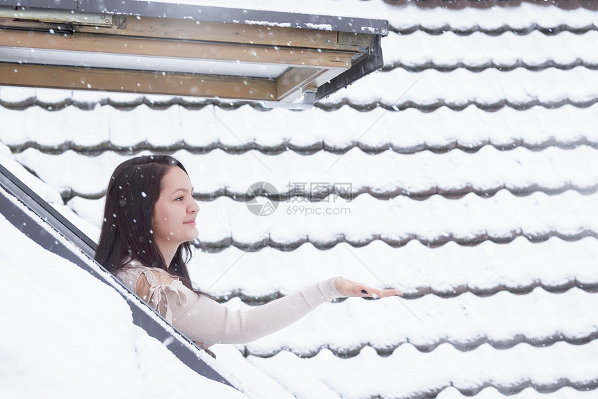 年轻美女站在窗口前用手接落下的雪花图片
