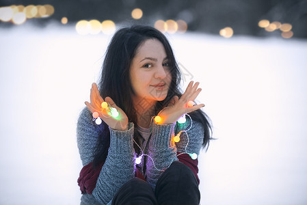坐在雪地上手握着多彩的亮绳子灯和他们一起玩耍图片
