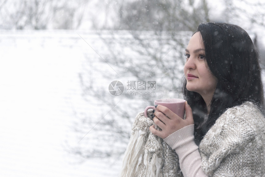 一个美丽的年轻黑发女人在下雪的时候喝热咖啡图片