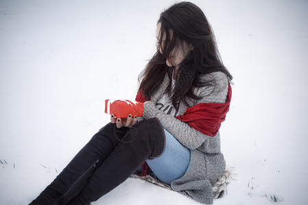 穿着高靴子寒冷的天气坐在雪地里手拿着一个红礼盒图片