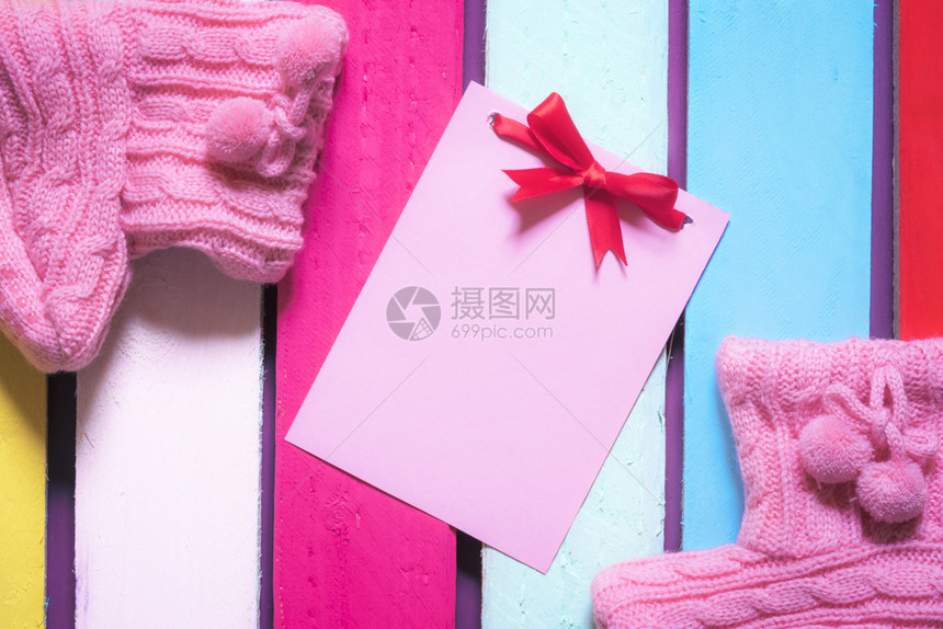 粉红色纸条弓周围是手工编织的粉红色靴子在多木制背景上图片