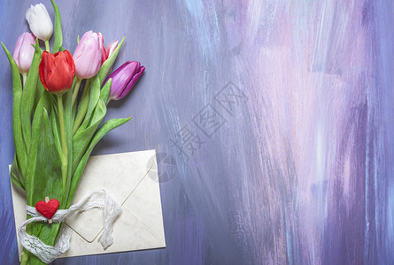 一束多彩的郁金香花束捆绑着带丝的彩色郁金香花一束红色心脏的木制剪片一包封装的信放在紫色木制背景的背景上背景图片