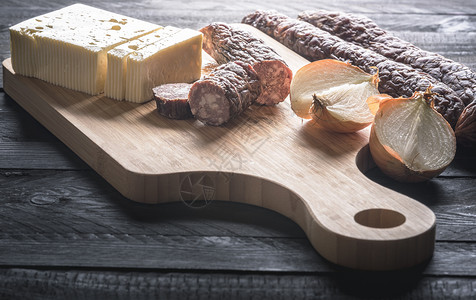 用自制的香肠和牛肉猪新鲜奶酪和洋葱放在木制切纸板上生锈的黑桌子上图片
