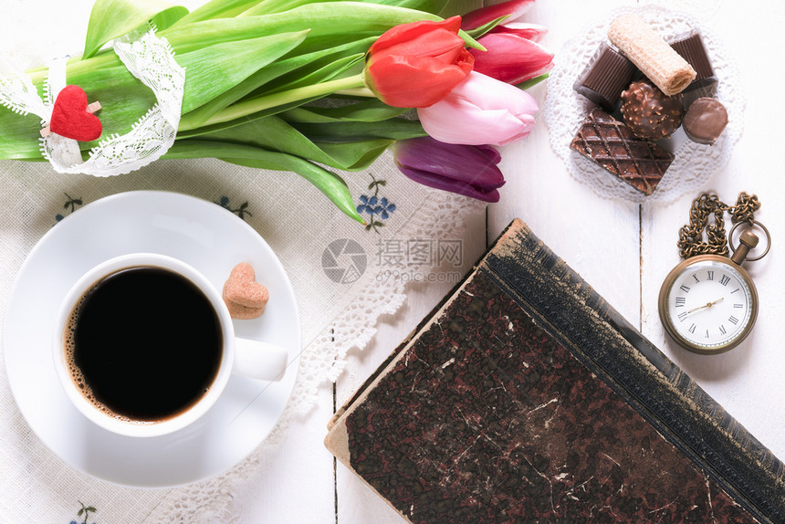 浪漫的早餐桌还有一杯咖啡甜点一本旧书时钟还有一束带蕾丝的郁金香花放在白桌上图片