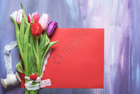美丽的花束彩色郁金香绑在白色的丝带和红心的木片放在一张空白的红纸页上图片