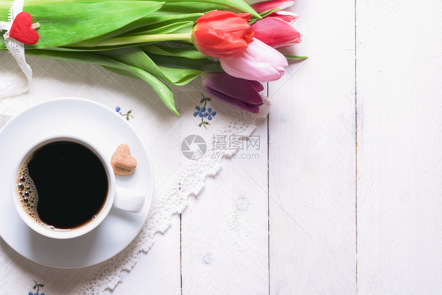 美丽的花束盛满多彩的郁金香绑着蕾丝一杯咖啡和心形糖放在古老的厨房毛巾上白木桌图片