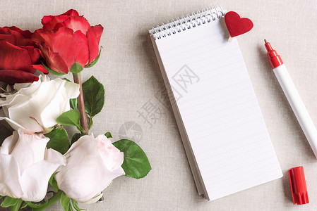 用条纹和红色心脏钉在笔记本上以及一束白玫瑰和红花束放在旧布料背景上图片