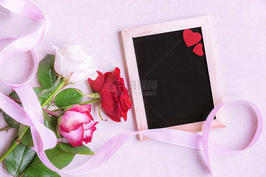 多色玫瑰花朵的可爱束与粉色丝带捆绑在一起紧靠个白黑板上面装饰着两颗红心在粉色背景上图片
