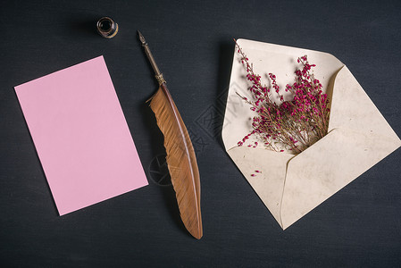 装满粉红色花朵的古老信封董笔墨水罐和空白信息卡黑木本底图片