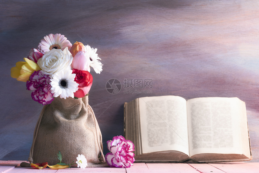 粉红色桌上的玫瑰花束雪贝拉郁金香和康乃馨还有一本古老的露天书靠在紫色木制背景上图片