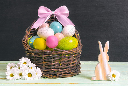粉兔子边框满是多色东方鸡蛋和粉弓的螺旋篮子周围着白菊花和木兔在一张桌子和堵黑墙上背景