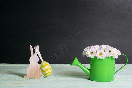 甜美的白菊花在水罐里和一只木兔挂着黄织物鸡蛋在绿桌和黑色背景上图片