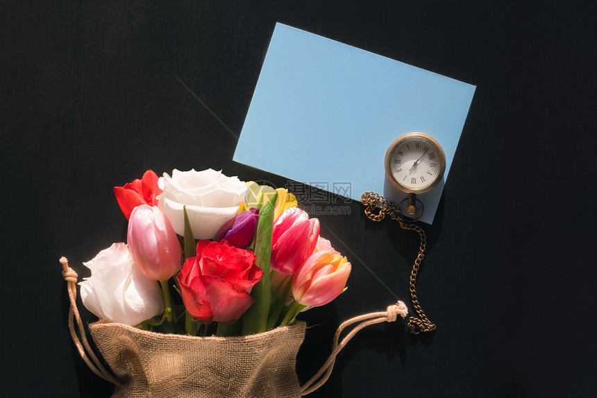黄麻袋里花朵多彩的束古老手表和一张空白的蓝色电文卡印在黑色背景上图片