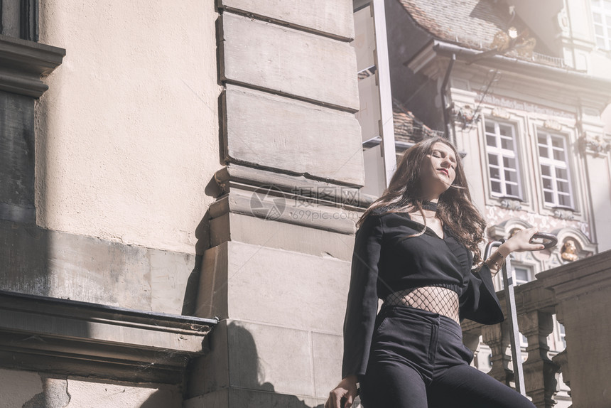 身着现代黑色衣服的有吸引力年轻女子仰赖着德国古老建筑环绕的巴勒斯贸易享受着阳光图片
