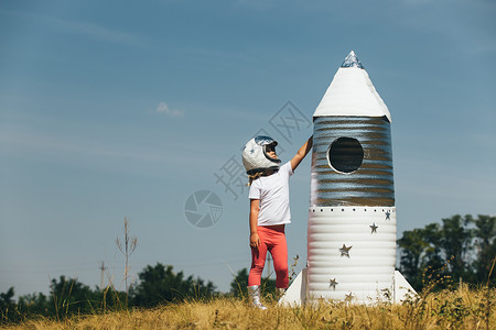 身着宇航员服装的快乐女孩玩着手制火箭夏天户外快乐女孩穿着宇航员服装的快乐女孩玩着手制火箭背景图片