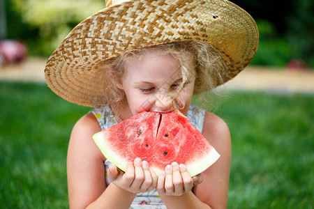 戴着草帽的小女孩在草地上吃西瓜图片