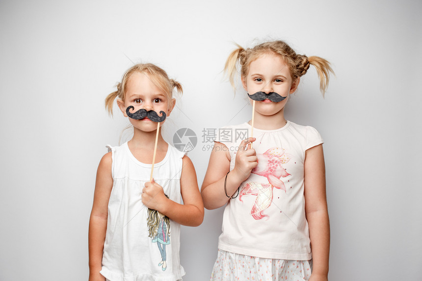 两个可爱的小女孩带着纸胡子身白色背景两个可爱的小女孩身着纸胡子图片
