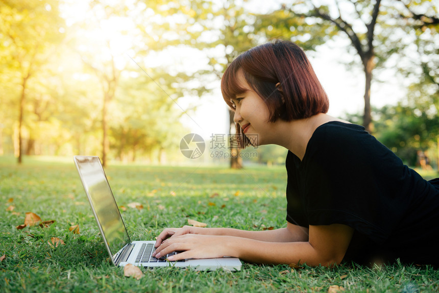 年轻的女用开放式笔记本电脑在绿草上双腿女孩和手放在键盘上远程学习概念在公园里工作笔记本电脑上快乐的时髦年轻女户外学习的生图片