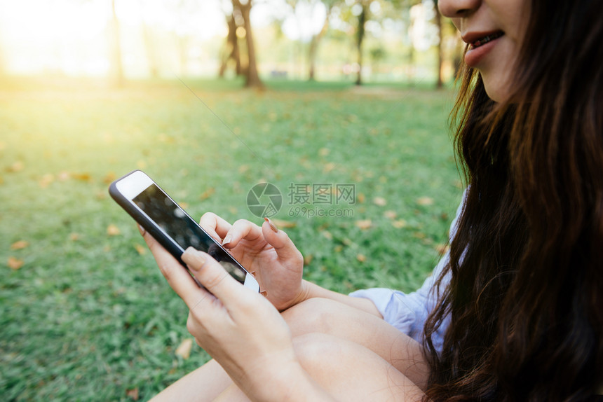 坐在公园春日时手机上读着愉快的短信图片