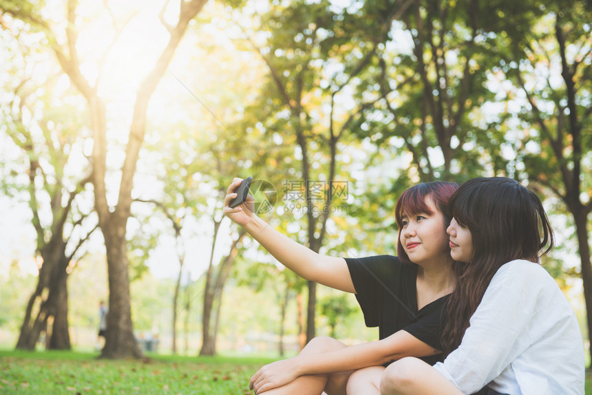 两个快乐的年轻亚洲女朋友一起在公园玩乐和自拍快的年轻亚洲女孩微笑看着智能手机生活方式和友谊概念图片