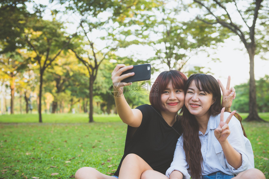 两个快乐的年轻亚洲女朋友一起在公园玩乐和自拍快的年轻亚洲女孩微笑看着智能手机生活方式和友谊概念图片