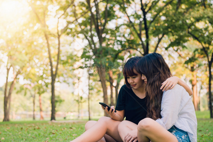 两个快乐的年轻亚洲女朋友一起在公园玩乐和自拍快的年轻亚洲女孩微笑看着智能手机生活方式和友谊概念图片