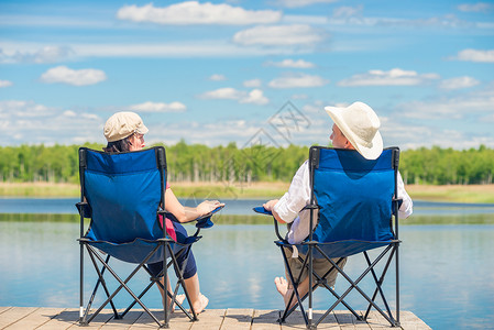 从一对夫妇的背面看坐在椅子上木头码的湖附近放松背景图片
