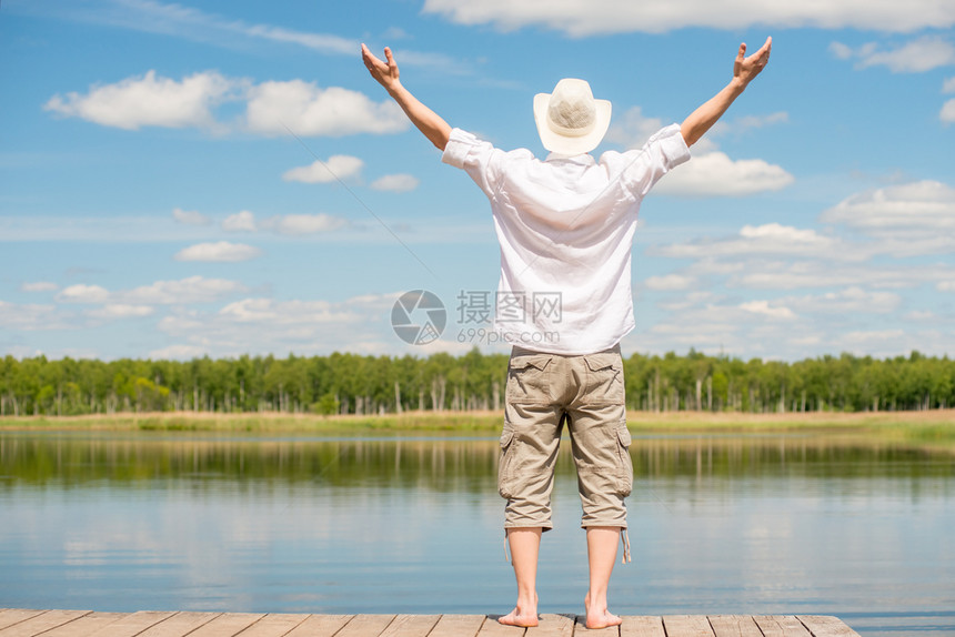 一个穿白衬衫的男人手伸在两侧享受湖边美丽的自然背面风景图片