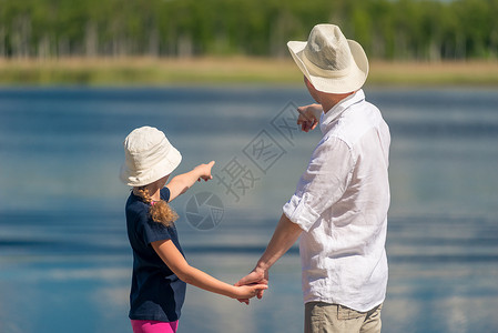 父亲和女儿在池塘附近的码头上用手指露水图片