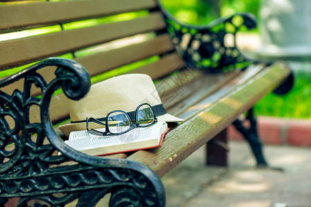 一本开放的新书时尚眼镜和草帽躺在公园长椅上图片