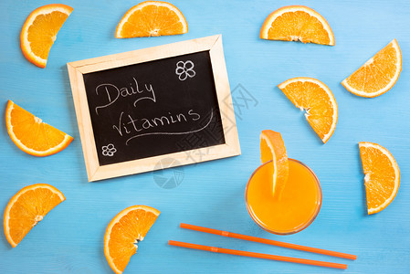 黑板的高角图像每天传递维他命信息周围是橙子片一杯果汁和稻草蓝底背景图片